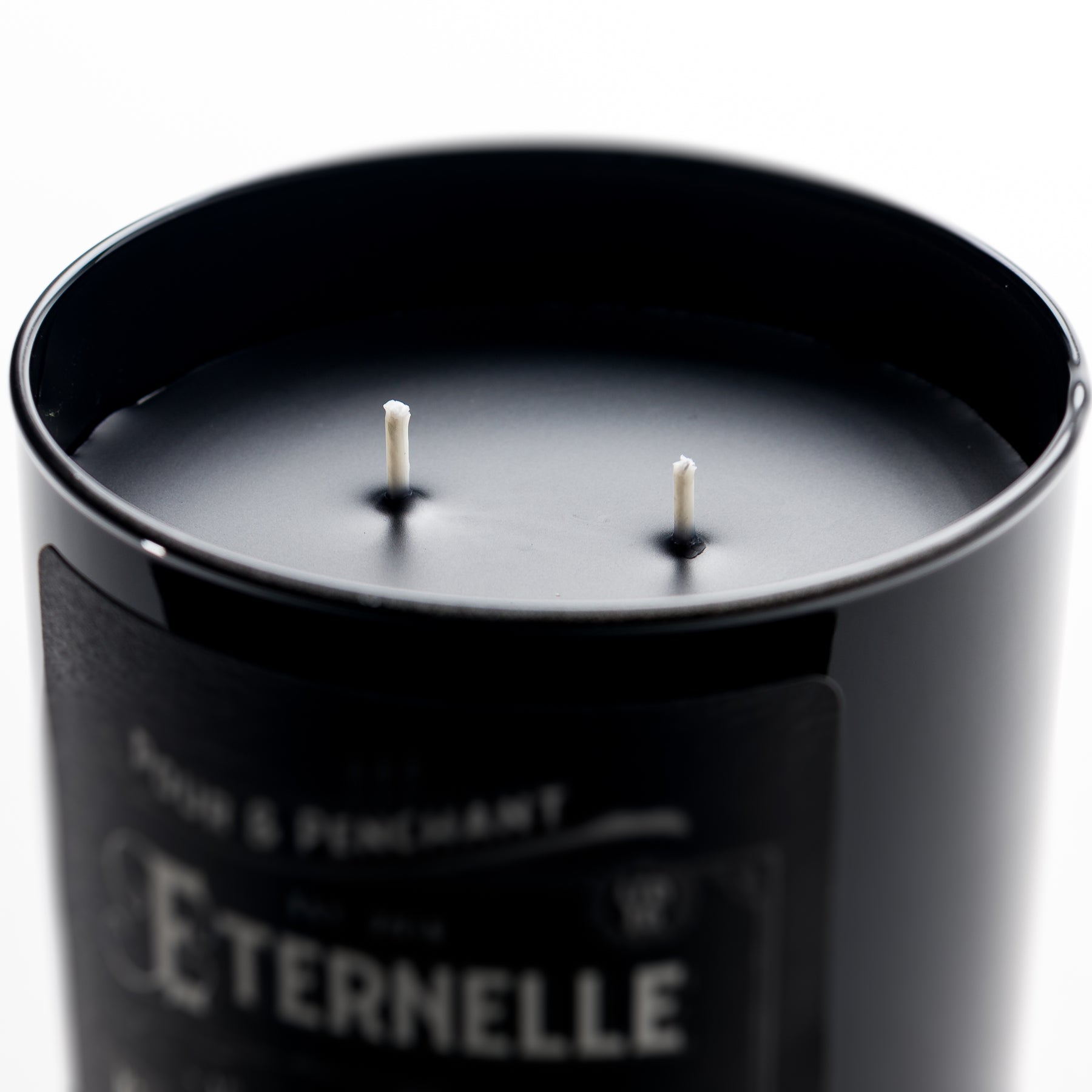 Close up image of a black candle vessel with two wicks and blurred background