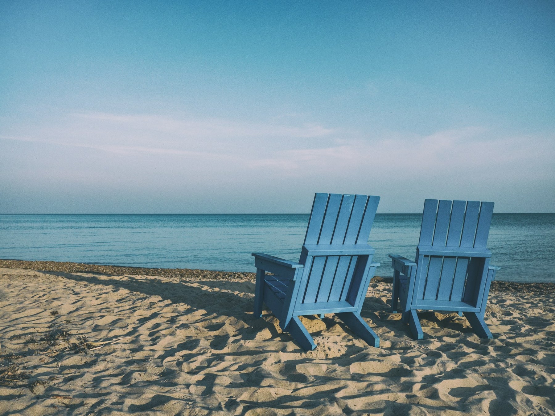Blue adirondack chairs on a beach overlooking the ocean