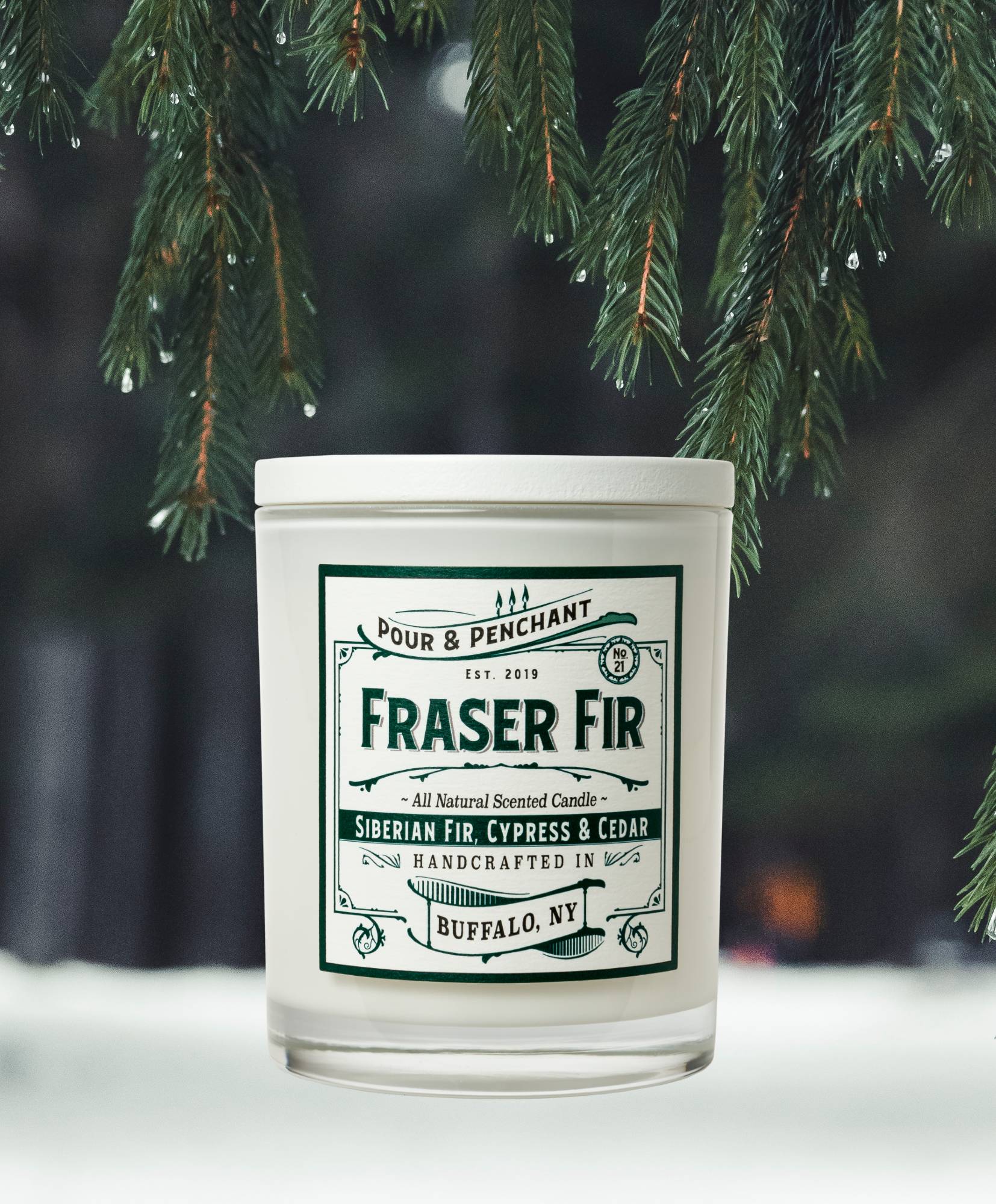 image of pour & penchant's bestselling holiday candle, fraser fir, set against a snowy background with pine needles